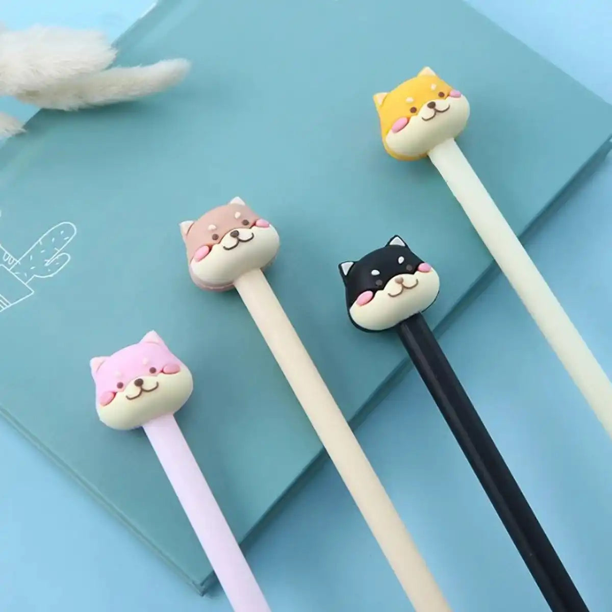 4 lápices en 4 colores distintos con caritas de perritos kawaii sobre un cuaderno y un fondo de color azul